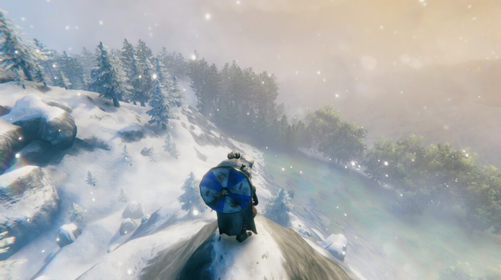 Screenshot from the game Valheim.
Char gazes down from a high hill, with snowy Mountain to the left and gentle, green Meadows to the right. It's sunny but quite hazy, giving the image a dreamy quality.